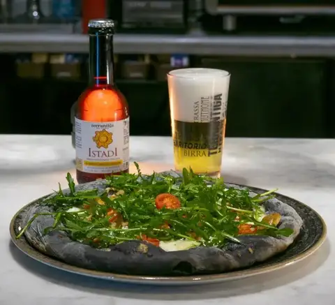 Pizza con impasto al carbone servita con birra artigianale eTrigu