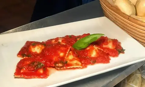 Ravioli al pomodoro con basilico su piatto bianco